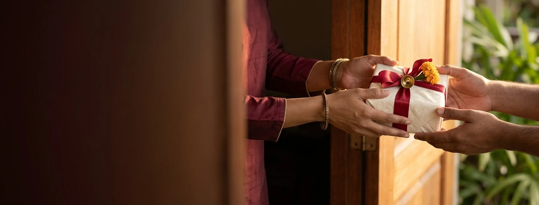 Hands passing a Diwali gift tied with ribbon and marigold promotion